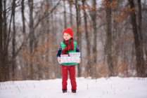 Хлопчик, що стоїть на снігу і несе різдвяні подарунки. — стокове фото