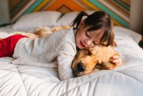 Jeune fille jouant avec le chien sur un lit — Photo de stock