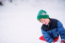 Lächelnder Junge spielt im Schnee auf die Natur an — Stockfoto
