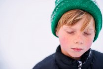 Retrato de um menino de pé na neve usando um chapéu de lã — Fotografia de Stock