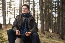 Man sitting in forest holding sunglasses — Stock Photo