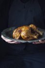 Person holding a Roast chicken on a pewter plate — Stock Photo