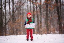 Junge steht im Schnee und trägt Weihnachtsgeschenke — Stockfoto