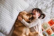 Giovane ragazza che gioca con il cane su un letto — Foto stock