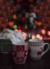 Two Christmas mugs in front of a Christmas tree — Stock Photo