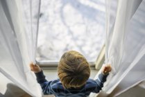 Хлопчик дивиться з вікна на сніг — стокове фото