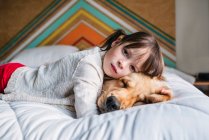 Chica joven jugando con el perro en una cama - foto de stock