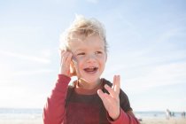 Lächelnder Junge, der am Strand steht und mit einem Mobiltelefon spricht, Orange County, Kalifornien, Vereinigte Staaten — Stockfoto