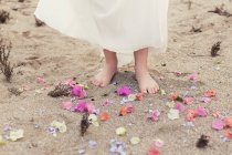 Girl standing barefoot in the sand surrounded by flower petals — Stock Photo