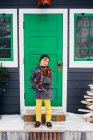 Menino em pé fora de uma casa segurando uma galinha — Fotografia de Stock