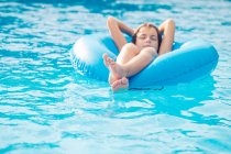 Menino que flutua em uma piscina em um anel de borracha inflável — Fotografia de Stock