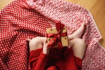 Вид сверху на девушку, сидящую со скрещенными ногами, держащую завернутый рождественский подарок — стоковое фото