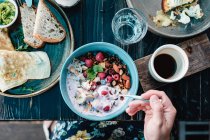 Mulher sentada em uma mesa de café da manhã comendo aveia com framboesas, nozes e sementes — Fotografia de Stock
