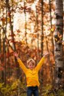 Мальчик бросает осенние листья в воздух — стоковое фото