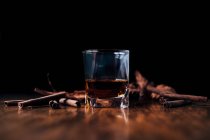 Whiskey con canela y hielo sobre fondo negro - foto de stock
