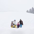Família em pé na neve segurando snowboard e trenó — Fotografia de Stock