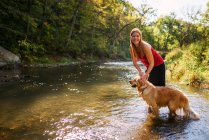 Woman standing in a river with a golden retriever dog — Stock Photo