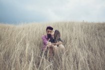 Женщина, сидящая в поле и целующая своего парня — стоковое фото