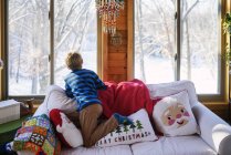 Vue arrière du garçon regardant par la fenêtre à la neige de Noël — Photo de stock