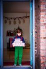 Boy standing in a doorway holding a stack of wrapped Christmas gifts — Stock Photo