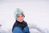 Retrato de un niño sonriente parado en la nieve - foto de stock