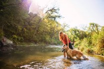 Mulher de pé em um rio com um cão golden retriever — Fotografia de Stock