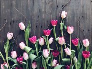 Tulipanes y ramitas rosadas sobre una mesa de madera - foto de stock