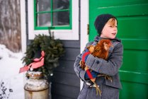 Garçon debout devant une maison tenant un poulet — Photo de stock