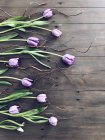 Красивые фиолетовые тюльпаны и веточки на деревянной поверхности — стоковое фото
