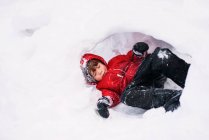 Ragazzo sdraiato in un buco nella neve all'aperto — Foto stock
