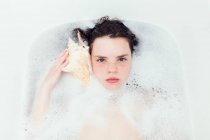 Дівчина лежить у бульбашковій ванні, слухаючи мушлю — стокове фото