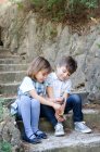 Niño y niña sentados en escalones jugando con conos de pino - foto de stock