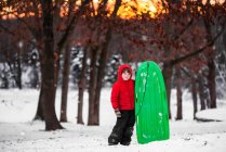 Junge steht im Schnee und hält Schlitten — Stockfoto