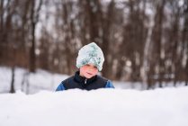 Мальчик, стоящий в лесу и строящий снежную крепость — стоковое фото