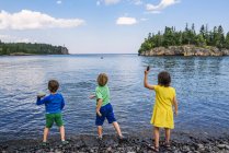 Three children throwing rocks into a lake — Stock Photo