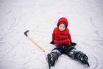 Мальчик сидит на льду с хоккейной клюшкой — стоковое фото
