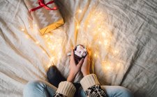 Mulher sentada em uma cama segurando uma caneca de chocolate quente com marshmallows — Fotografia de Stock