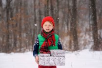 Garçon debout dans la neige portant des cadeaux de Noël — Photo de stock