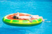Мальчик лежит на надувном арбузе в бассейне — стоковое фото