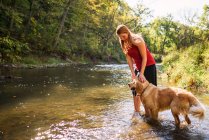 Woman standing in a river with a golden retriever dog — Stock Photo