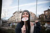 Woman sitting on a swing eating a lollipop — Stock Photo