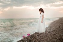 Девушка стоит на пляже в белом платье — стоковое фото