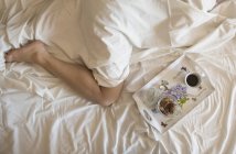 Bandeja de pequeno-almoço ao lado de uma mulher na cama, vista elevada — Fotografia de Stock