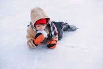 Garçon allongé sur un lac gelé portant des patins à glace mangeant de la glace — Photo de stock
