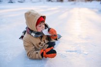 Junge liegt mit Schlittschuhen auf einem zugefrorenen See und isst Eis — Stockfoto