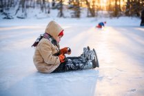 Junge sitzt mit Schlittschuhen auf einem zugefrorenen See — Stockfoto