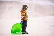 Menino em pé no lago congelado segurando um trenó — Fotografia de Stock