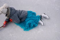 Girl lying on a frozen lake holding a hockey stick — Stock Photo
