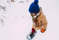 Garçon marchant dans la neige portant des raquettes — Photo de stock