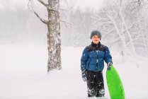Ragazzo in piedi con una slitta nella neve pesante — Foto stock
